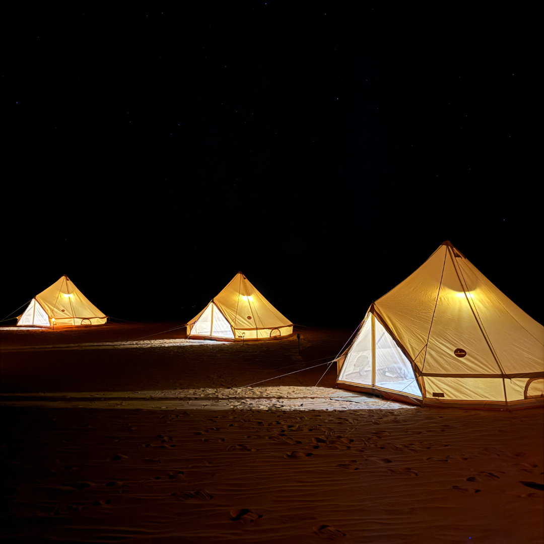 Three Bedouin bell tents lit up across the sand at night