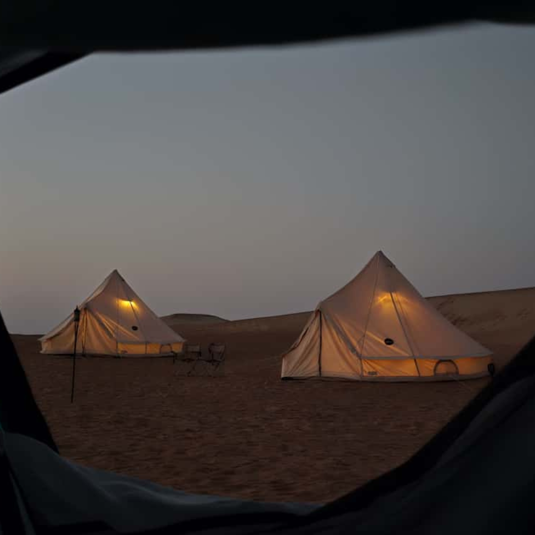 Two Bedouin bell tents lit at dusk, seen from a tent doorway