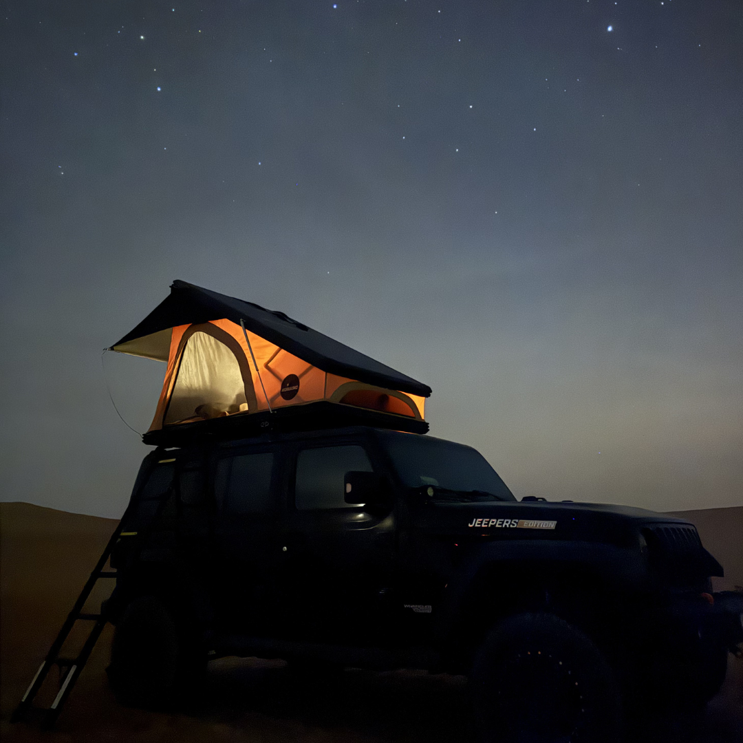 The Nomad rooftop tent glowing from inside under a starry night sky