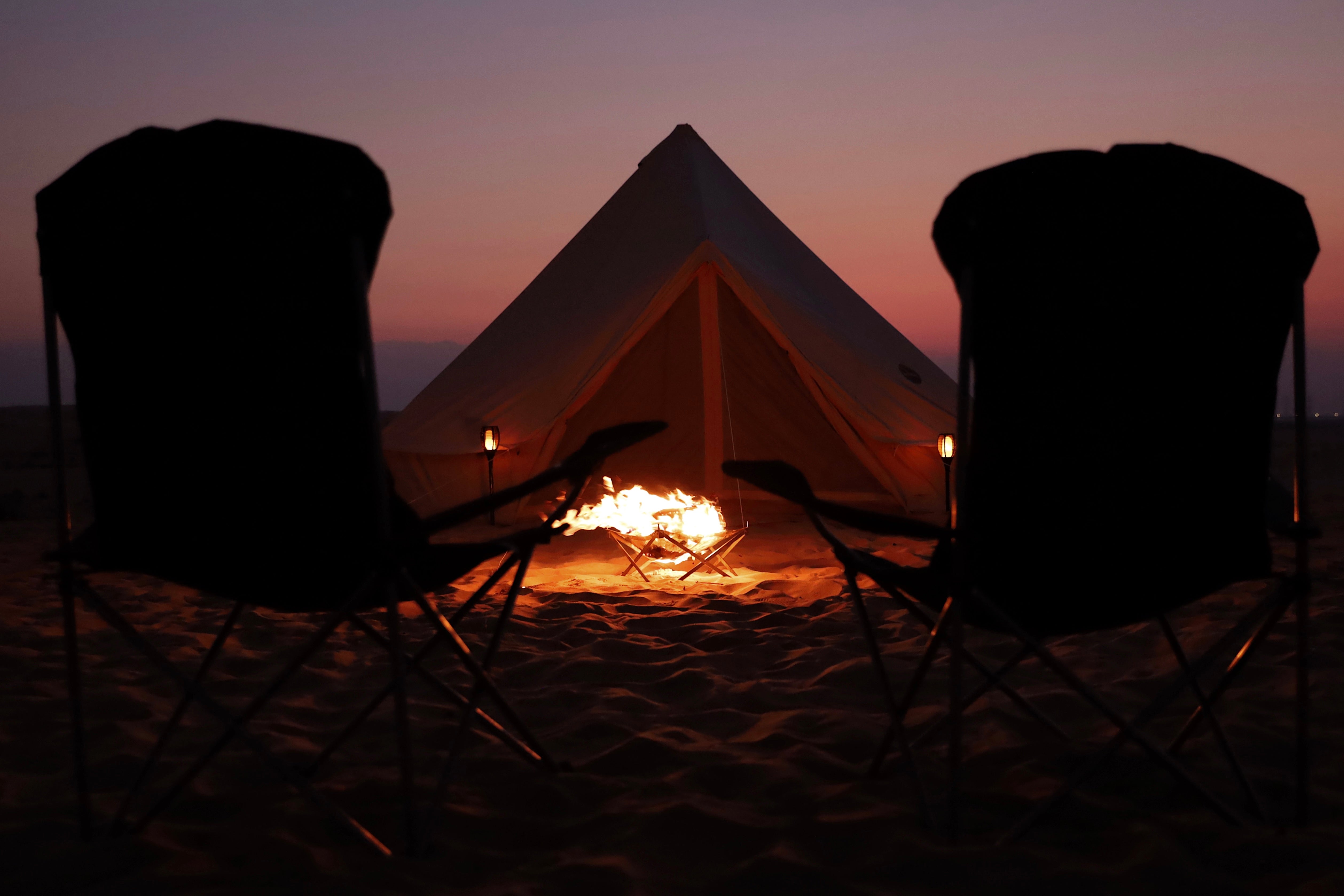 Camp chairs and a fire at twilight outside a lit Nomadic bell tent